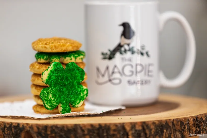 Stacked sandwich cookies with green icing beside a Magpie Bakery bag